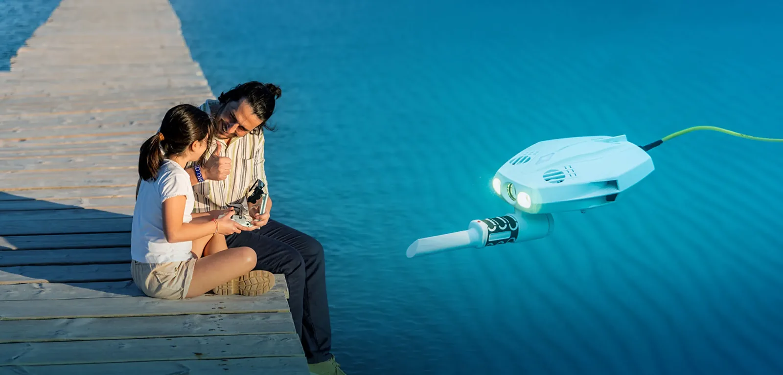 CHASING Dory Explore mit Metalldetektor-Stab unter dem Gehäuse schwebt im Wasser, zwei Personen mit Fernbedienung sitzen auf einem Steg