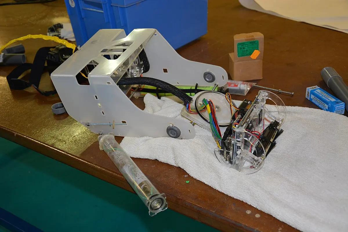 Halb montiertes OpenROV auf einer Werkbank: weißer Kunststoffrahmen, leere Acrylröhre im Vordergrund, daneben der Elektronikträger mit Platinen und bunten Kabeln
